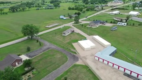 Aerial view of rural farm property with large white storage buildings, red barn, driveway, and green pastures