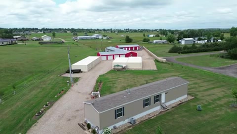 Aerial view of rural farm property with red and white barn, metal building, and surrounding green fields