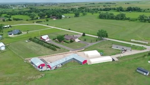 Aerial view of rural farm with red barn, white agricultural buildings, and green fields